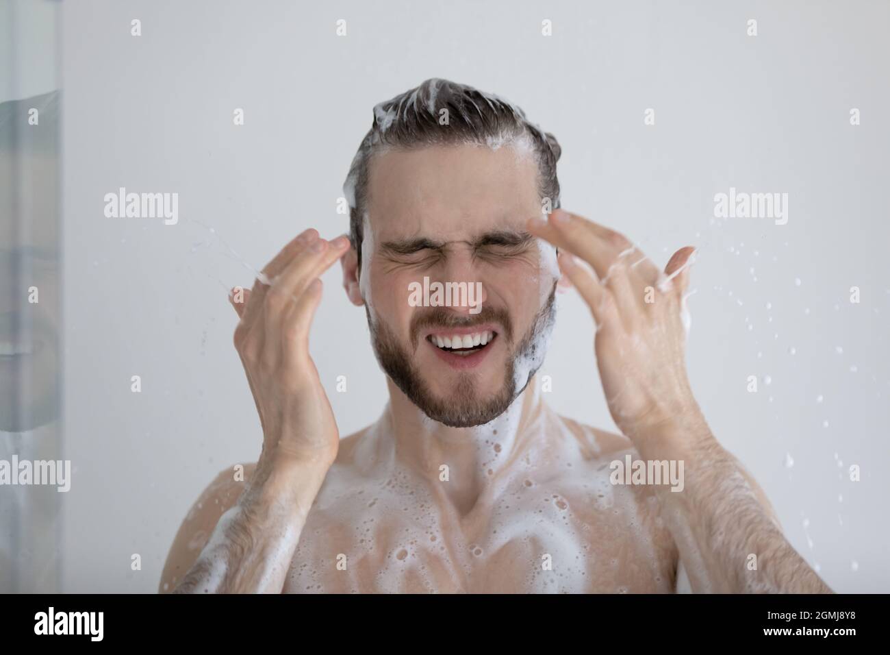 L'homme prend une douche avec les yeux déchirant en raison du shampooing au sulfate Banque D'Images