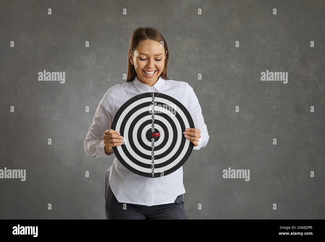 Jeune femme souriante tenant la cible de tir avec la flèche rouge de dart à droite dans le logo de la cible Banque D'Images