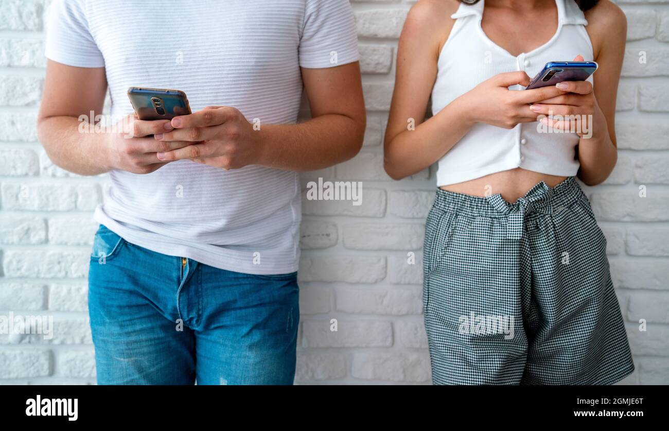 Deux amis ou amoureux debout face à awall et regardant leurs téléphones mobiles. Concept de dépendance technologique. Photo de haute qualité Banque D'Images
