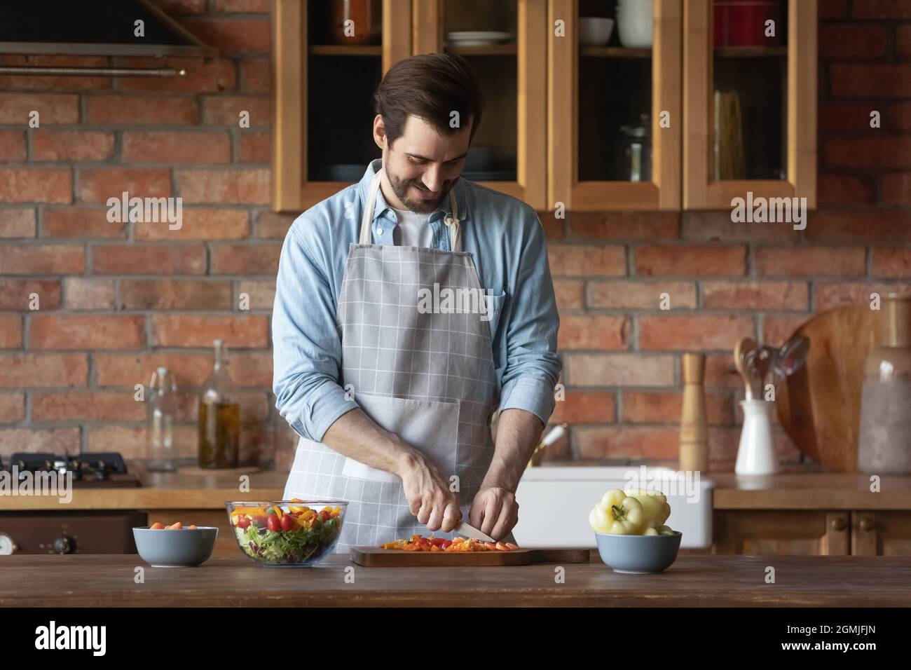 Homme souriant en tablier coupant des légumes, cuisinant à la maison Banque D'Images