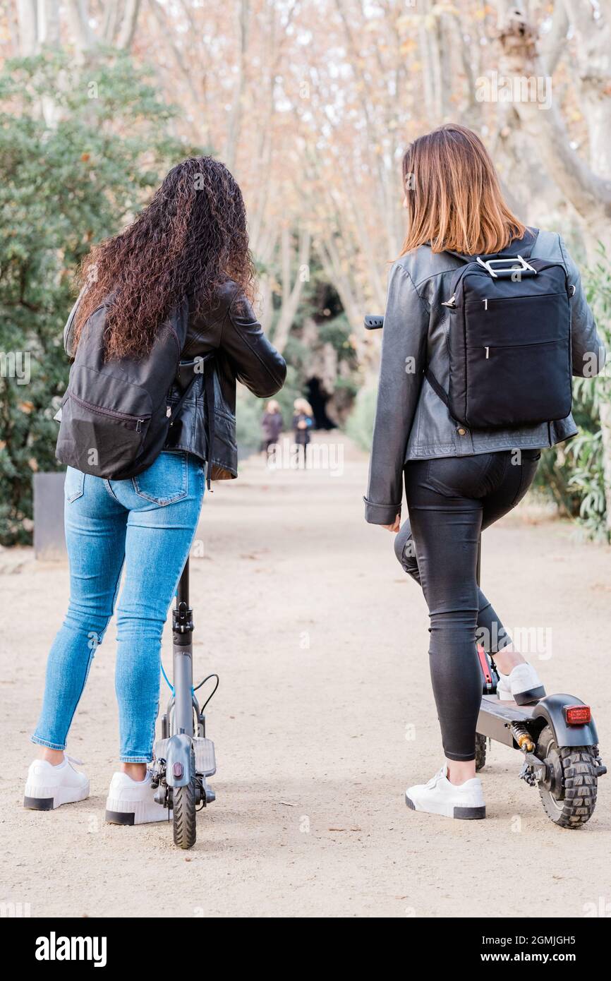 Vue arrière de deux amies multiethniques sur des scooters électriques. Mode de vie urbain et concepts de transport écologique Banque D'Images