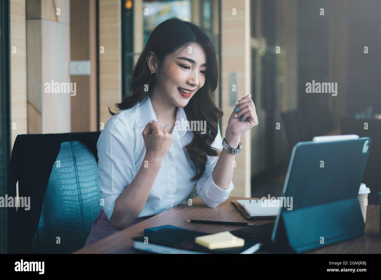 Une femme asiatique excitée s'assoit à son poste de travail, extatique d'avoir reçu une offre d'emploi à la suite d'un entretien par e-mail sur son ordinateur portable Banque D'Images