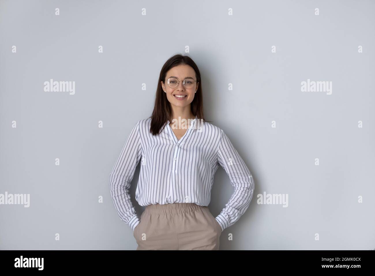 Portrait confiante femme en lunettes debout sur fond gris Banque D'Images