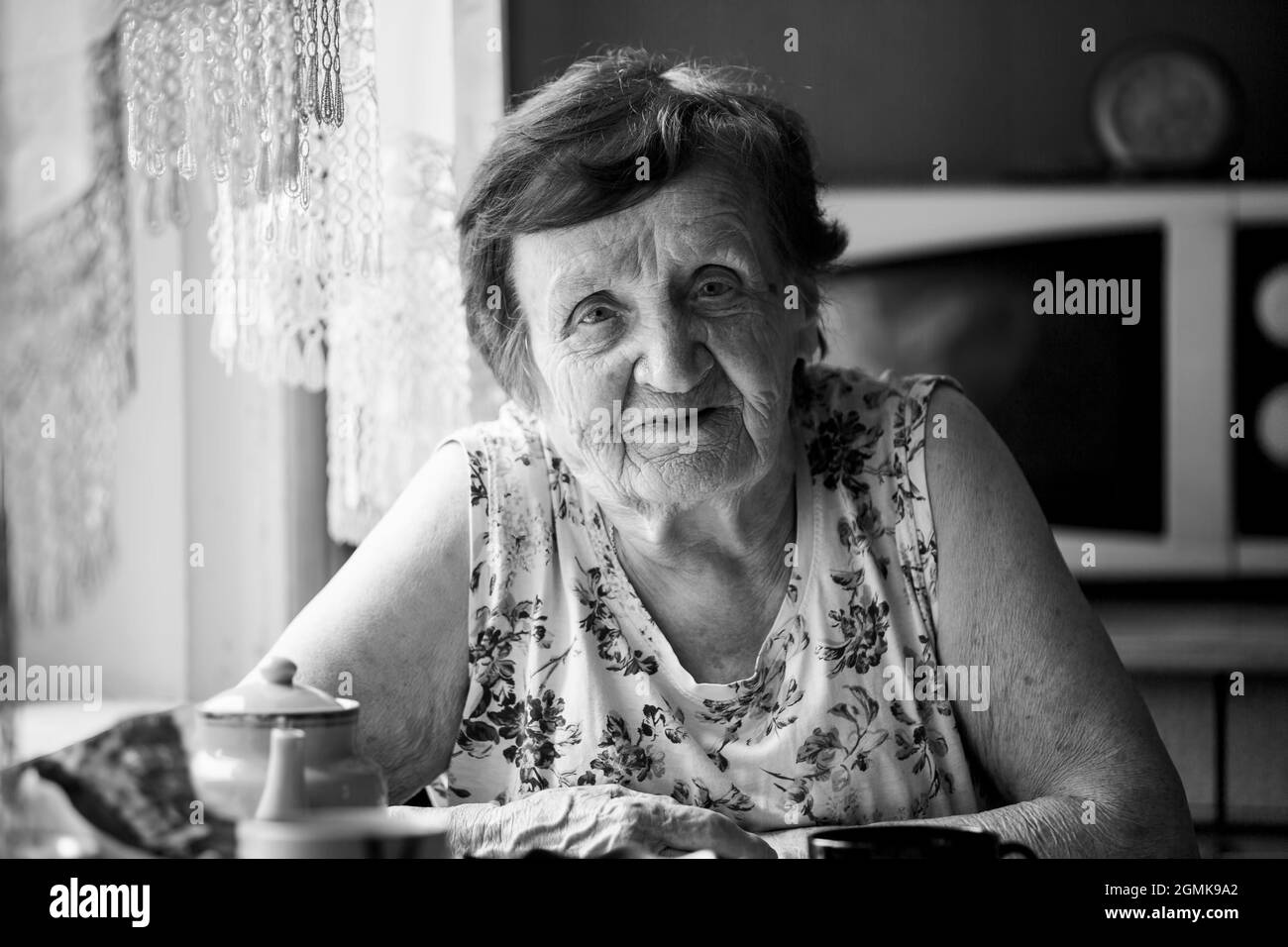 Portrait d'une vieille femme assis à une table dans sa maison. Photo en noir et blanc. Banque D'Images