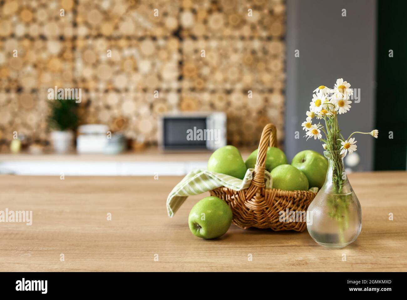 Panier avec pommes vertes fraîches et vase avec fleurs sur table dans la cuisine Banque D'Images
