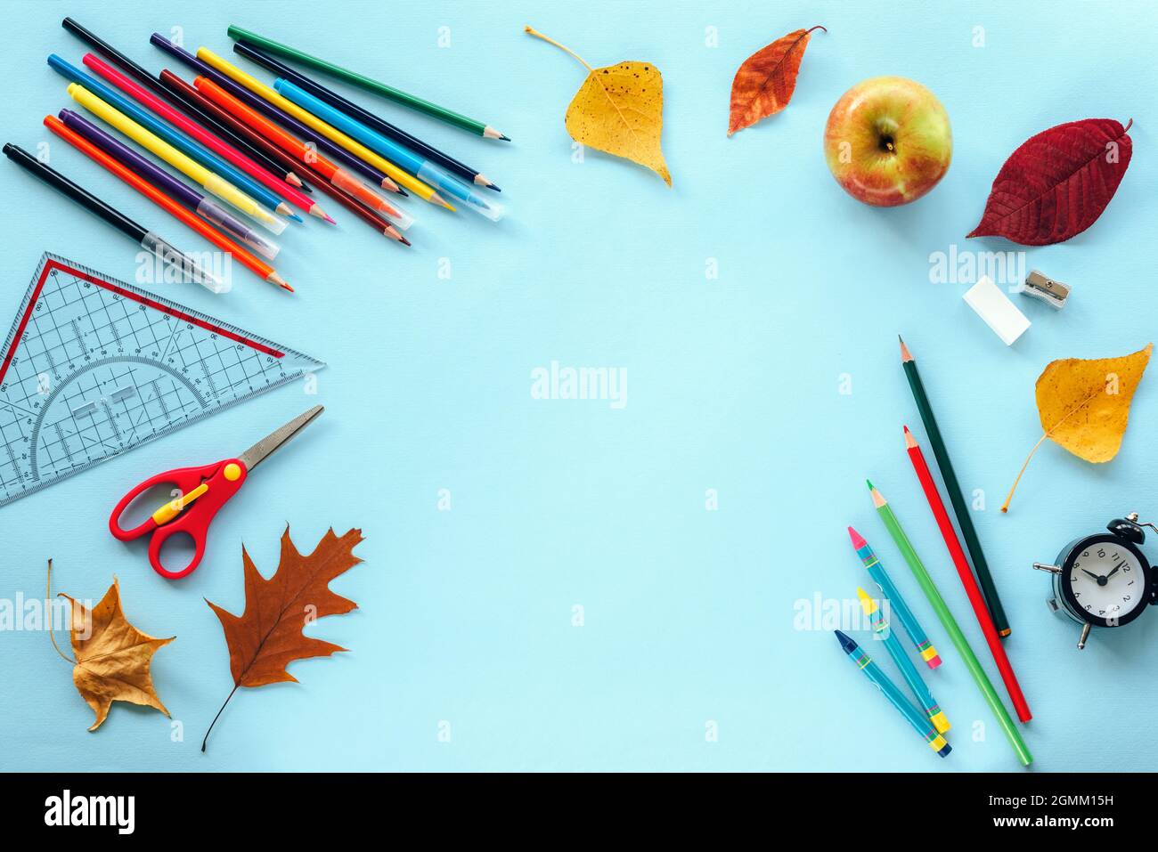 Fournitures scolaires papeterie, crayons de couleur, ciseaux, règle, réveil, pomme, feuilles d'automne sur fond bleu. Concept de retour à l'école. Vue de dessus Banque D'Images