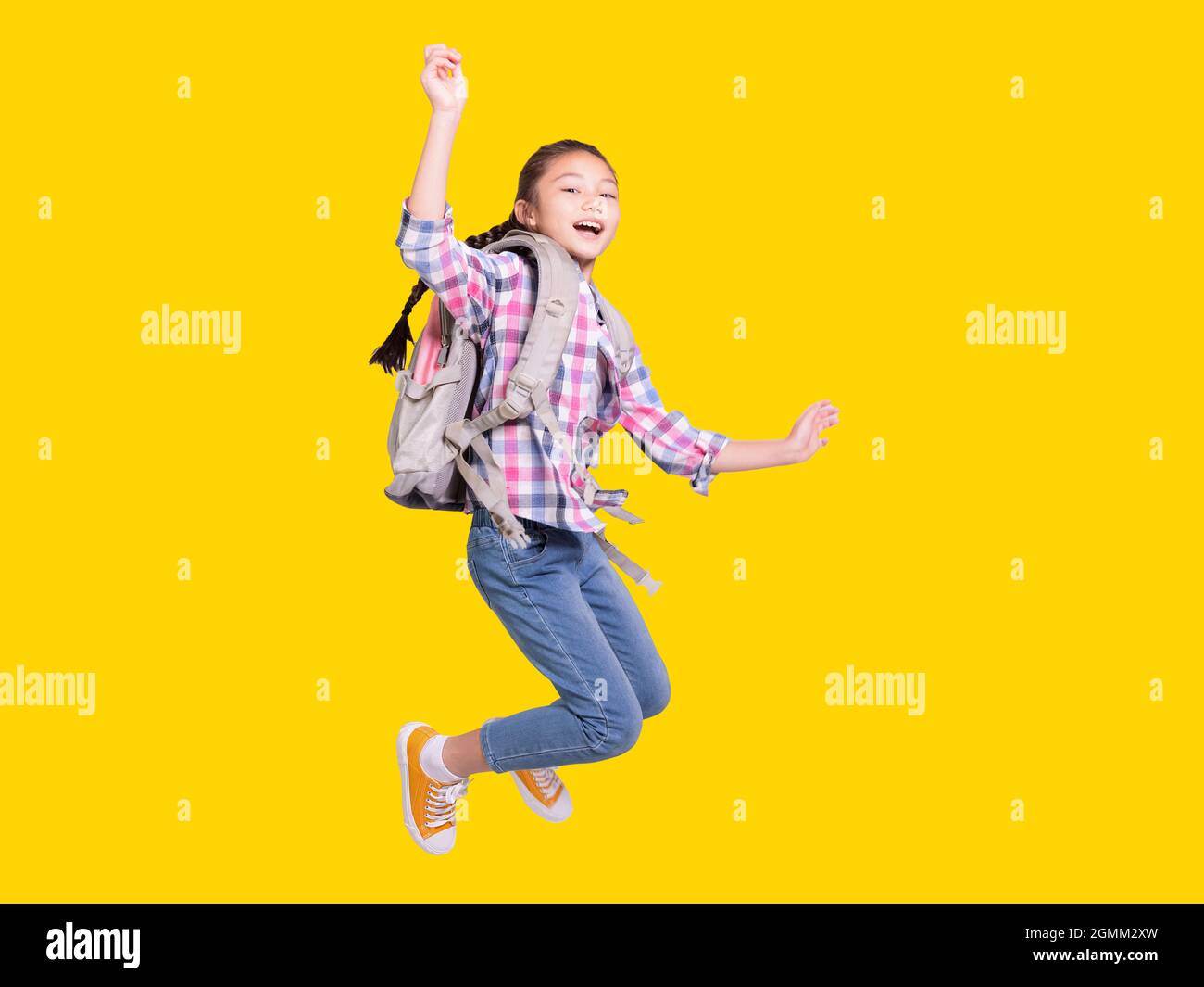 Portrait d'une fille étudiante heureuse avec sac et saut.isolé sur fond jaune. Banque D'Images
