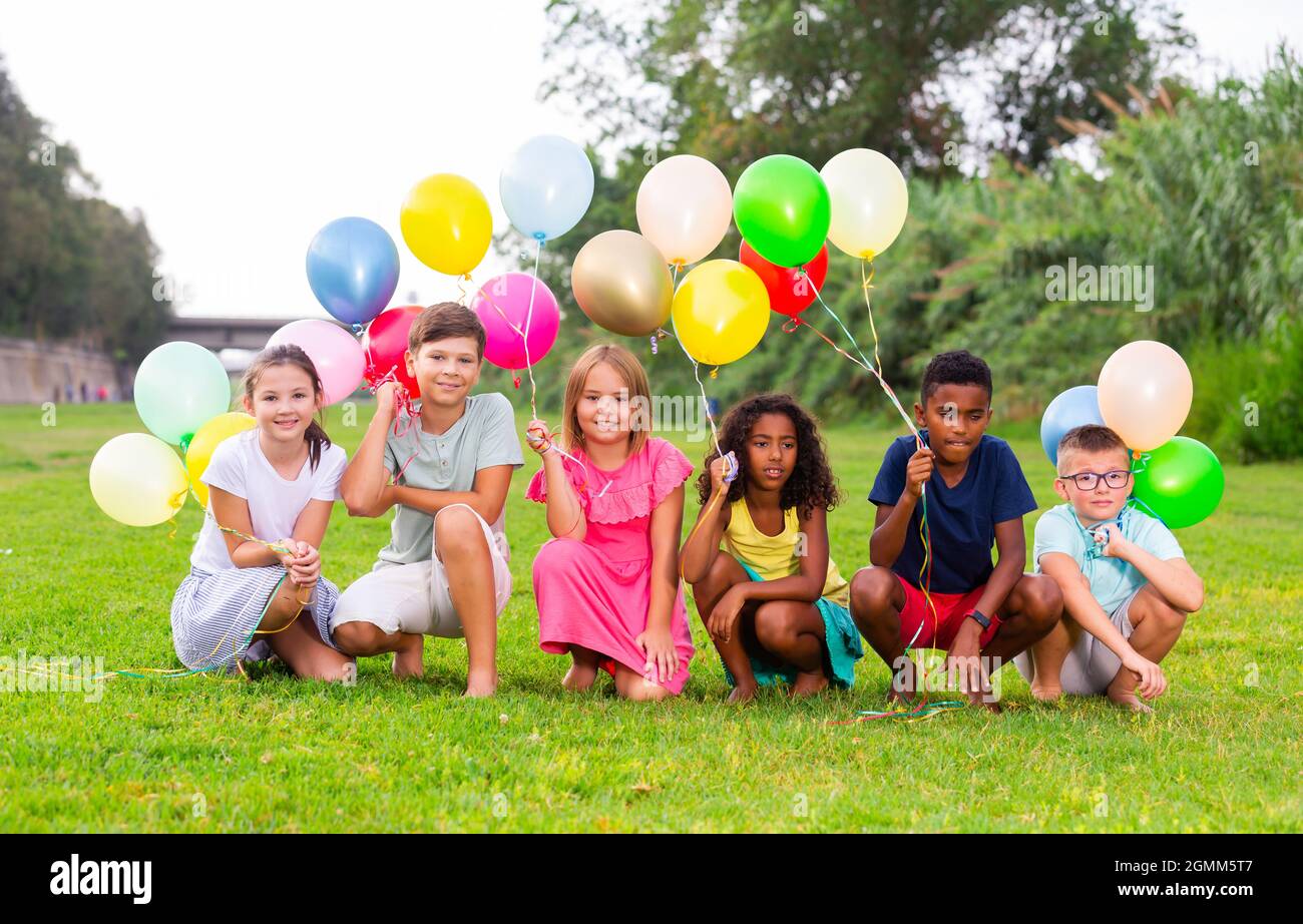 Joyeux préadolescents garçons et filles avec des ballons colorés sur la pelouse verte Banque D'Images