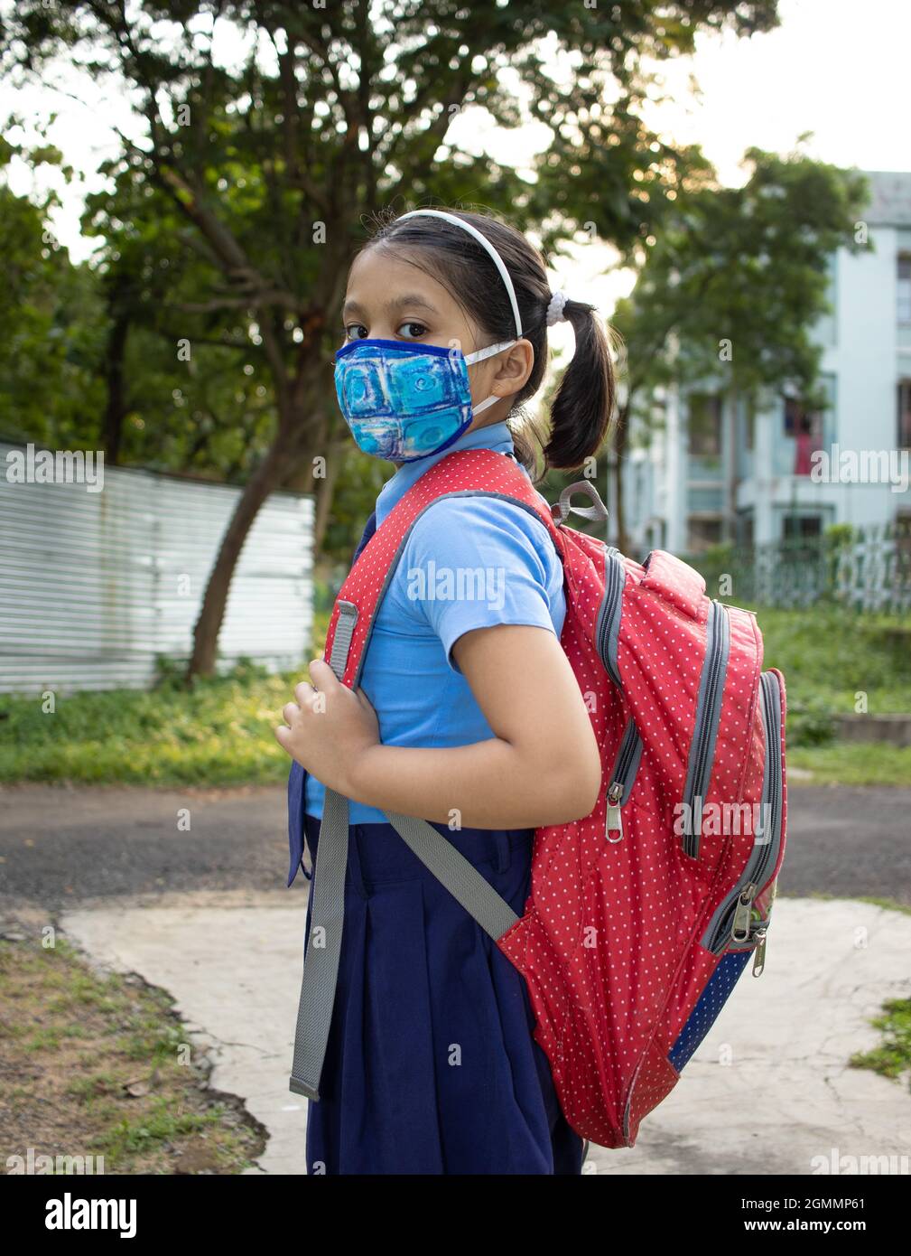 Portrait d'une jeune fille indienne heureuse en uniforme scolaire bleu avec sac rouge et masque de protection allant à l'école Banque D'Images