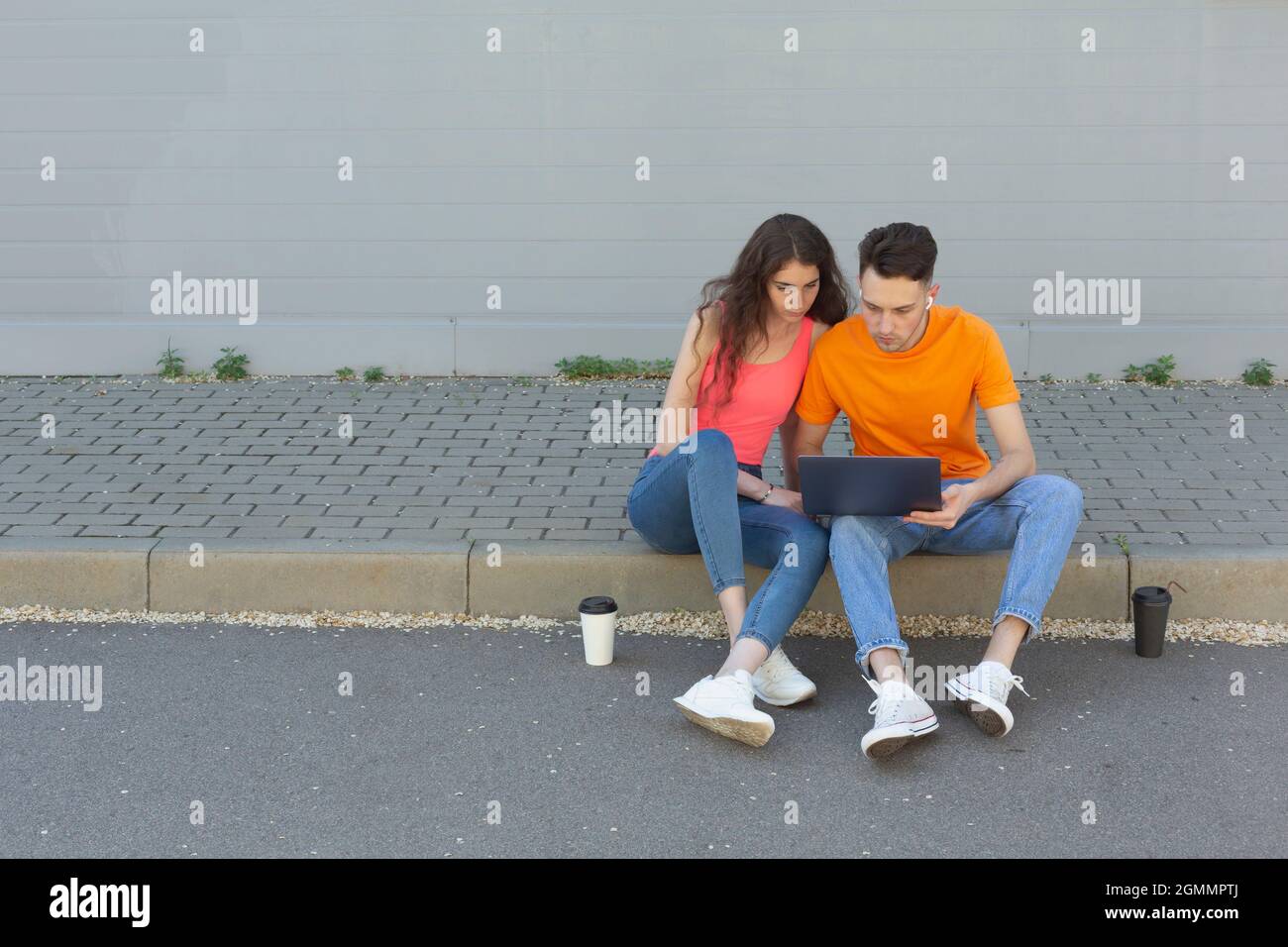 Jeune couple utilisant un ordinateur portable sur le trottoir Banque D'Images