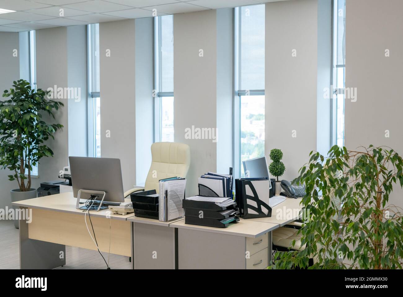 Deux bureaux avec écrans d'ordinateur et documents se tenant le long des  fenêtres dans un grand bureau à espace ouvert Photo Stock - Alamy