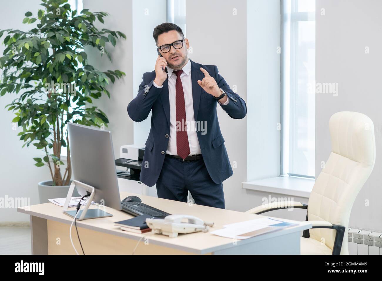 Employeur confiant en costume élégant discutant des conditions de l'accord au téléphone tout en restant debout près de son lieu de travail Banque D'Images