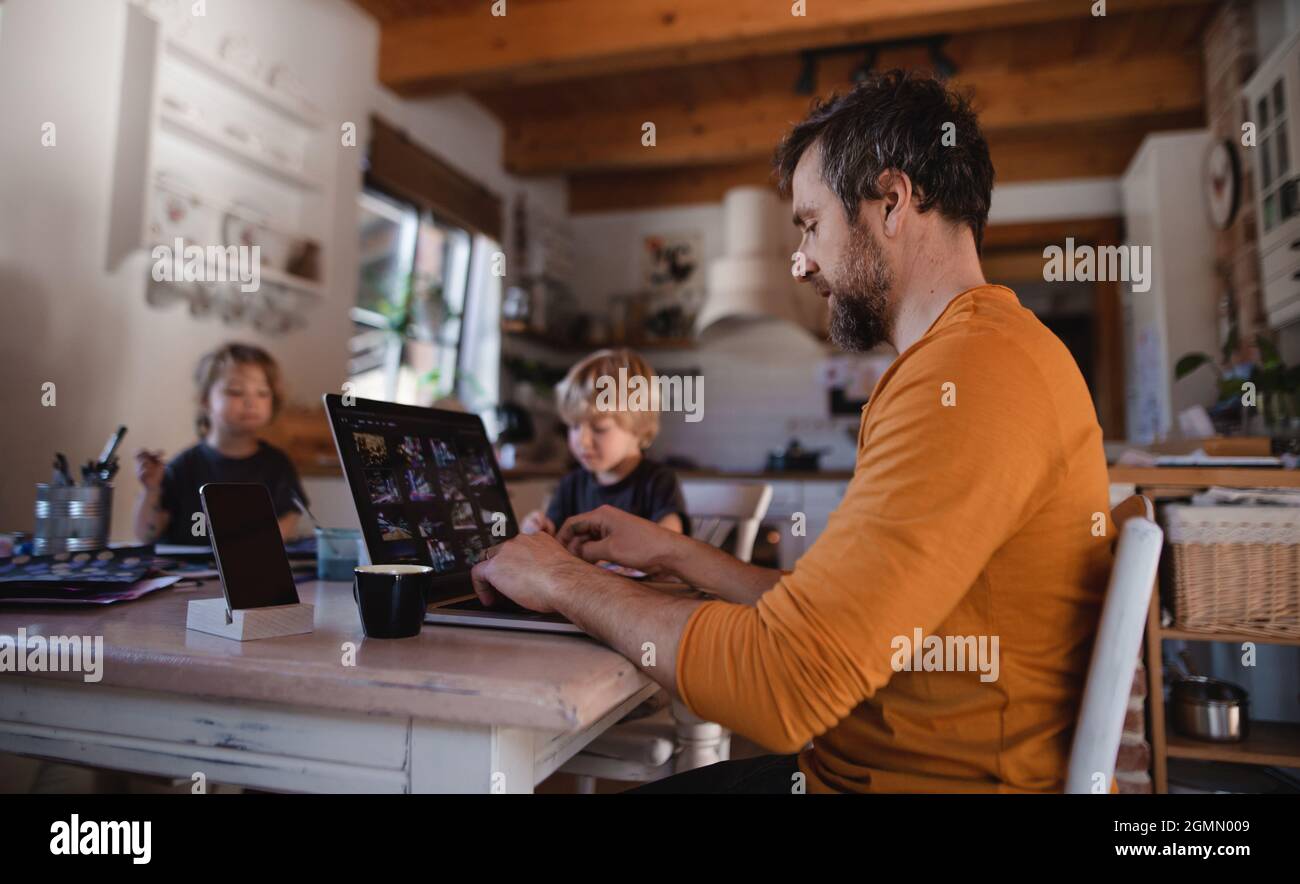 Père adulte moyen avec deux petits enfants travaillant à l'intérieur à la maison, peindre des photos et le concept de bureau à la maison. Banque D'Images