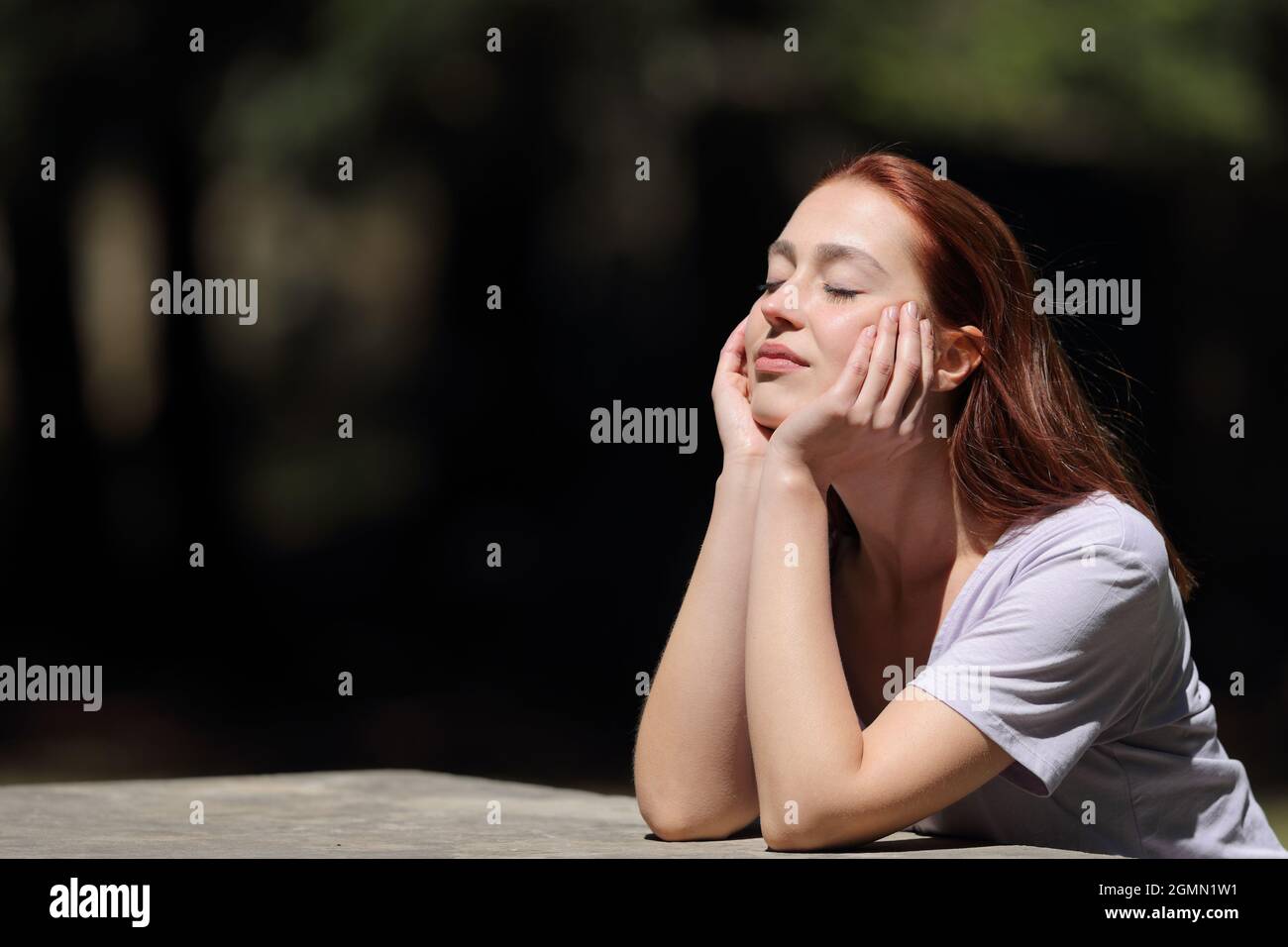 Femme aux yeux fermés se détendant et chauffant une journée ensoleillée dans un parc Banque D'Images