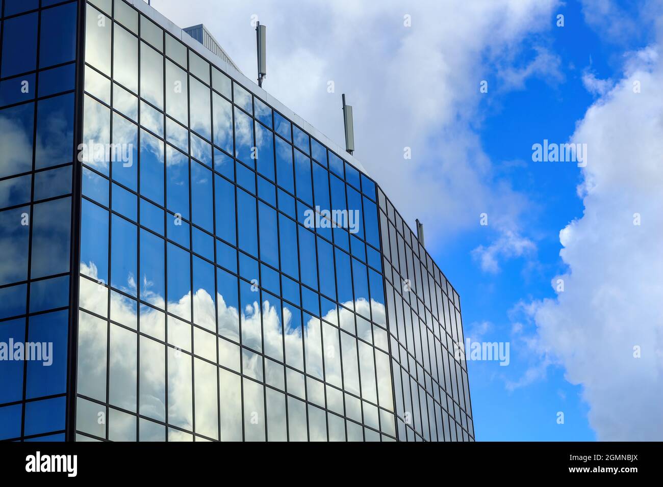 Ciel bleu et nuages moelleux reflétés dans les fenêtres d'un bâtiment en miroir Banque D'Images