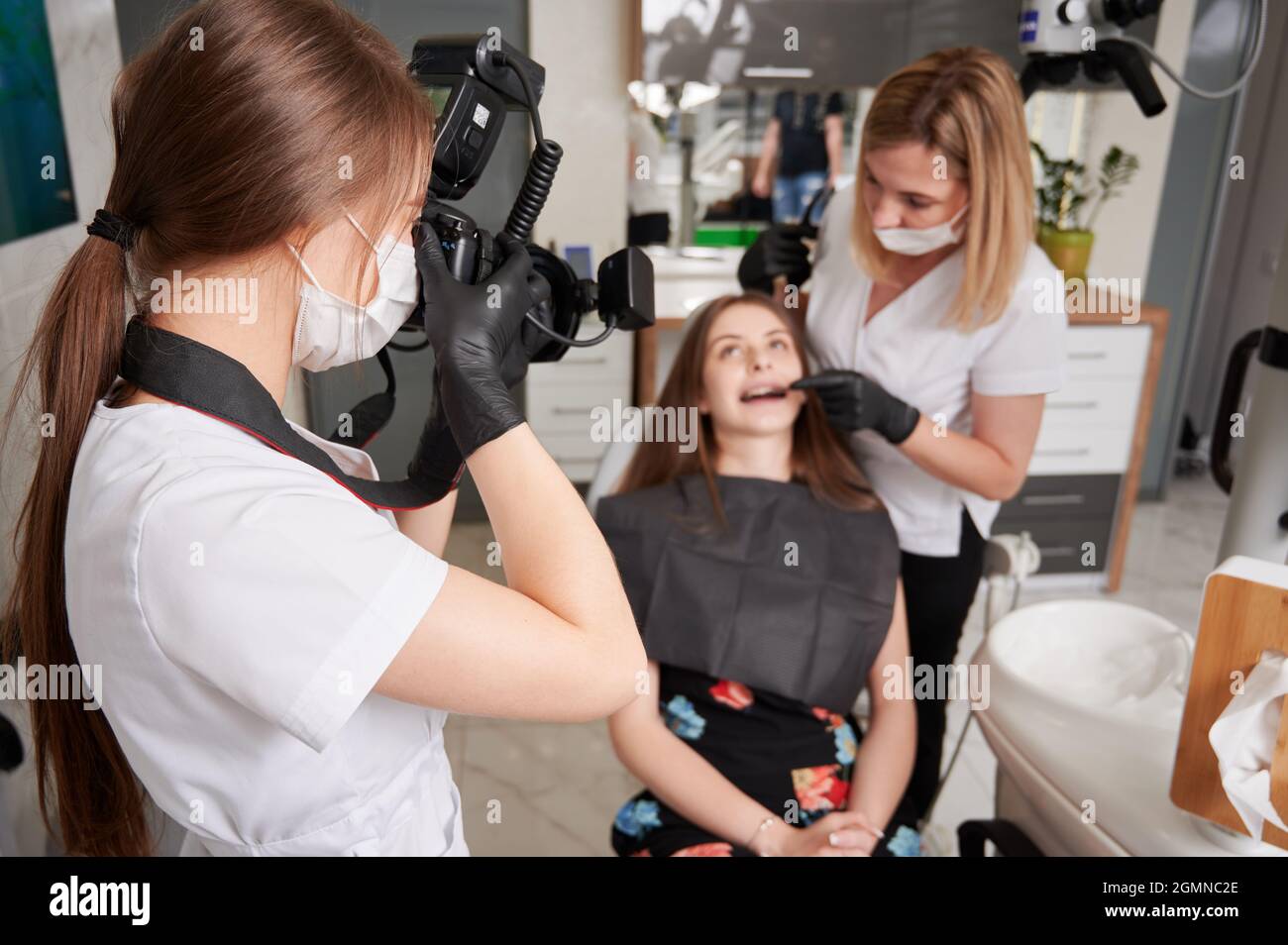 Dentiste examinant les dents de la femme pendant qu'assistant dans le masque médical prenant des photos avec un appareil photo professionnel. Jeune femme médecin en gants stériles photographiant le patient et le dentiste au cabinet dentaire. Banque D'Images