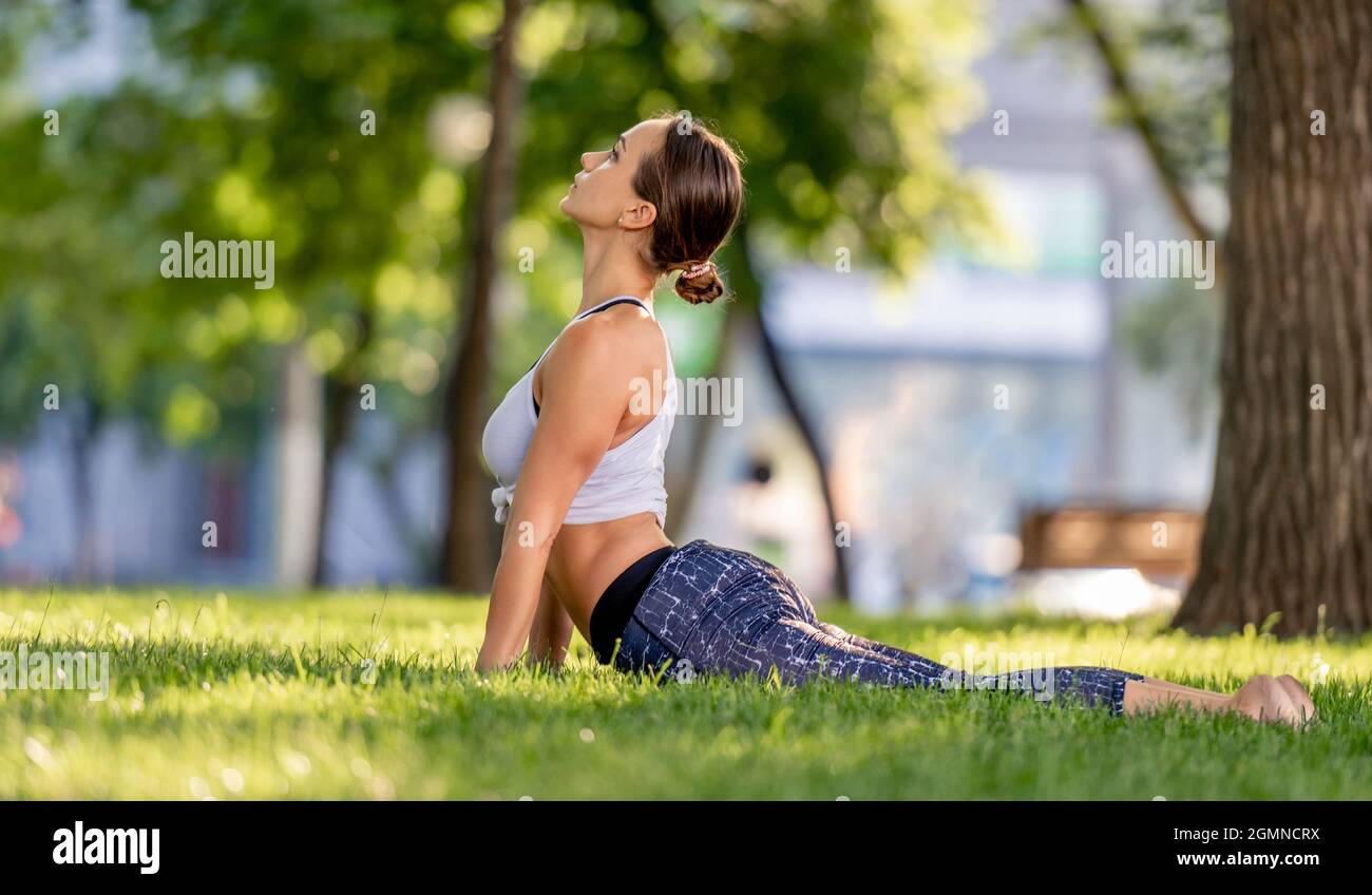 Fille faisant du yoga à la nature et debout dans la posture du chien vers le haut sur l'herbe. Jeune femme s'exerçant et stertching en été Banque D'Images