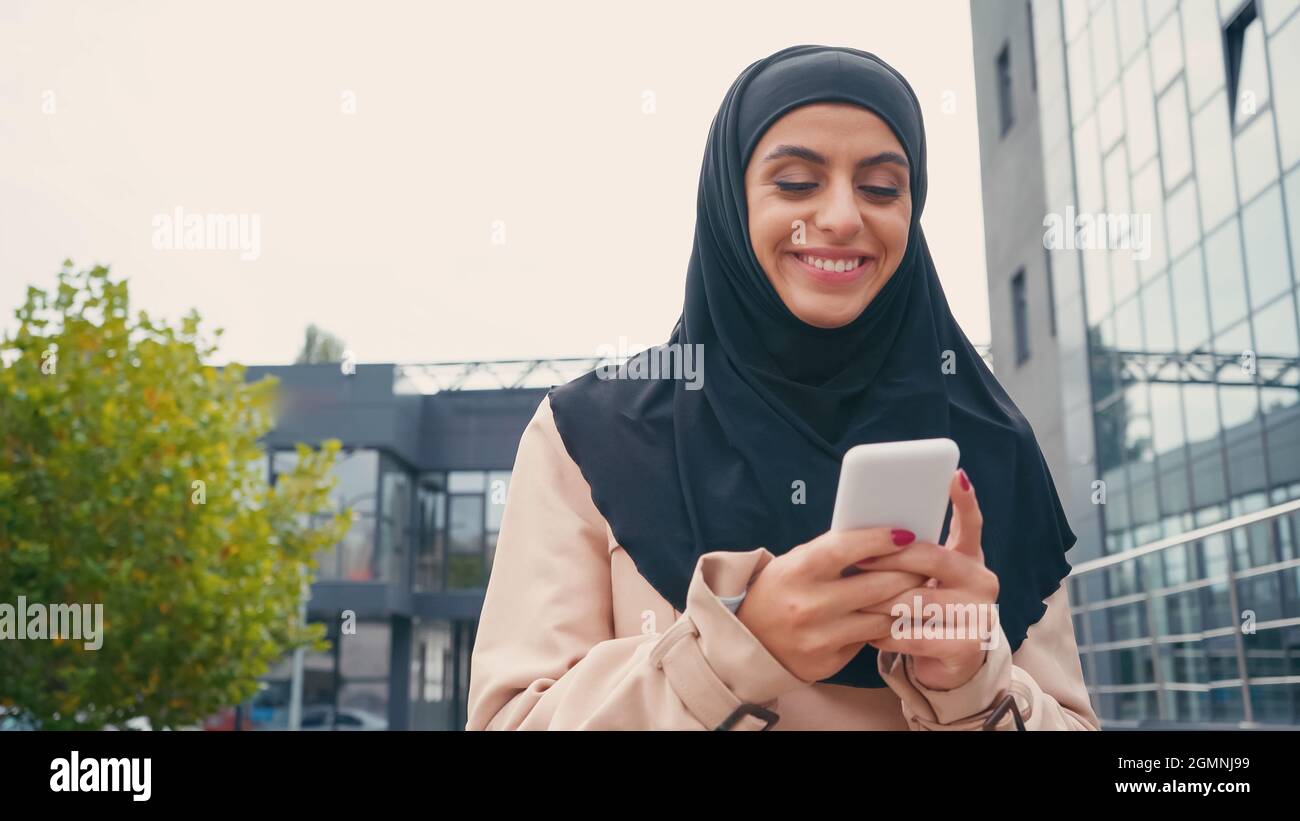 jeune femme musulmane joyeuse dans un message hijab sur un téléphone mobile à l'extérieur Banque D'Images