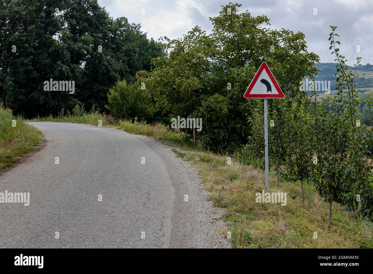 Virage à gauche sur une route, avec un signal d'avertissement pour un virage serré à gauche Banque D'Images