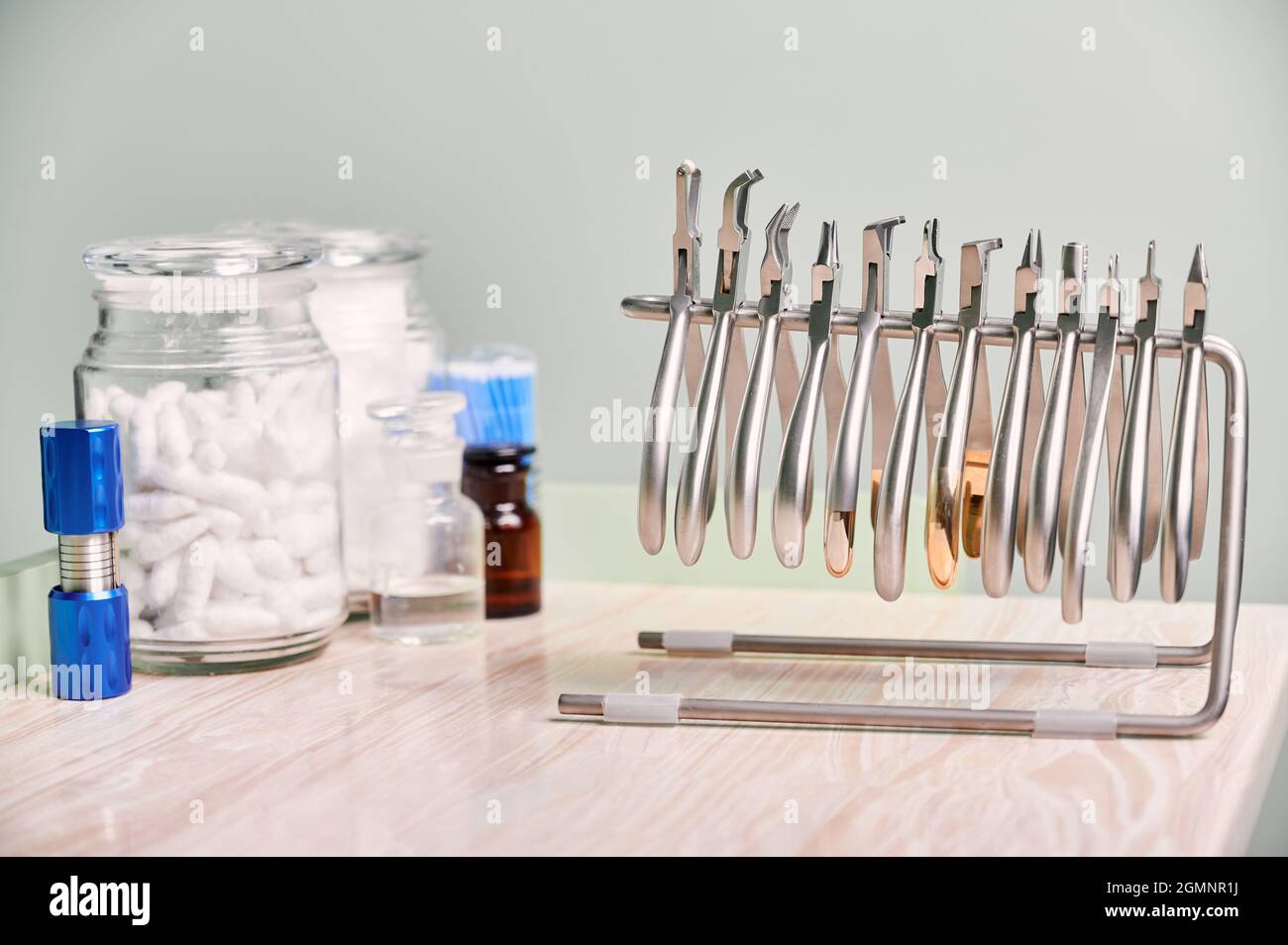 Jeu de différents instruments en acier inoxydable pour bretelles et jarre de rouleaux de coton dentaire dans le bureau de stomatology. Pinces, pinces coupantes, dissolvants et autres outils orthodontiques argentés sur table en bois. Banque D'Images