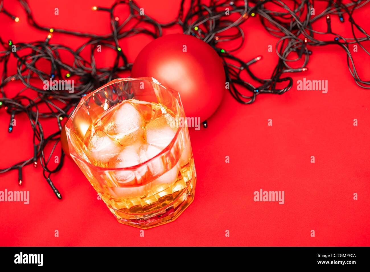 Verre de whisky avec glaçons et décoration de noël sur fond rouge - concept boisson de noël Banque D'Images
