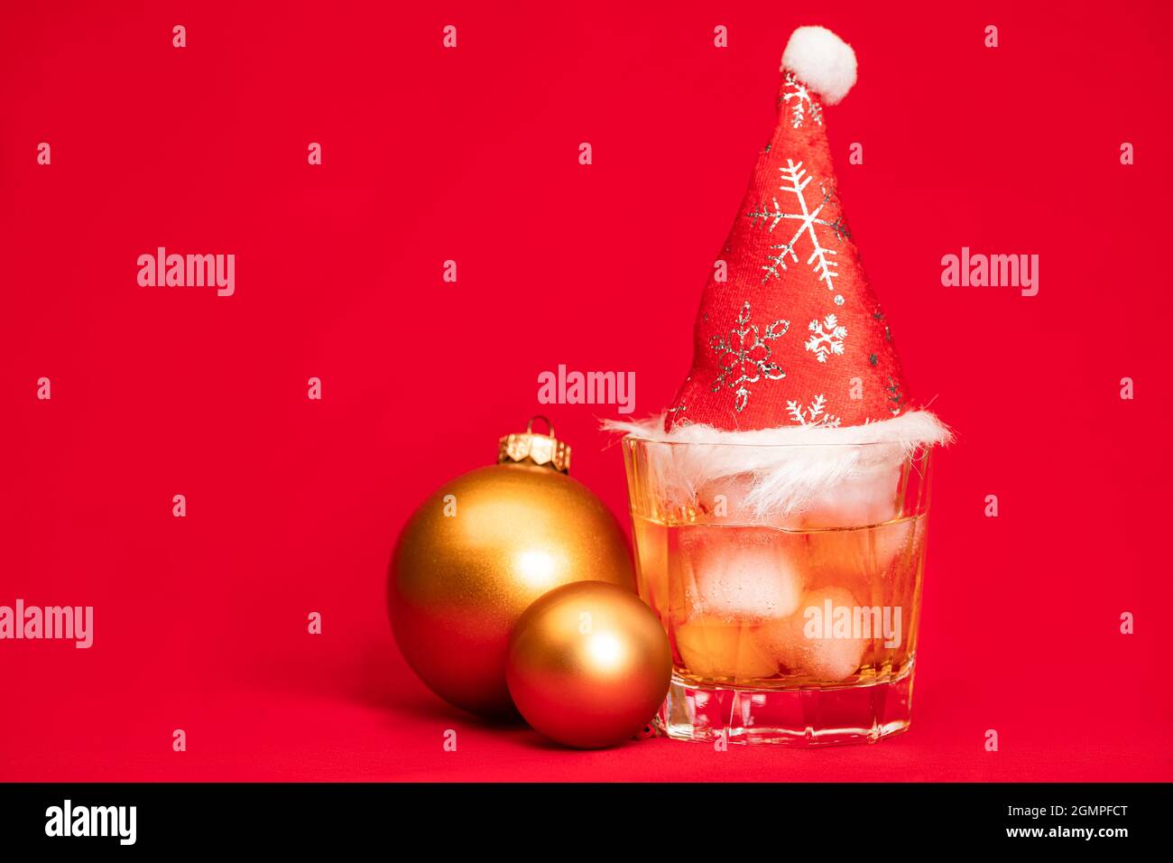 Verre de whisky sur les rochers avec chapeau de père noël rouge et boules de noël sur fond rouge - concept de boisson de noël Banque D'Images