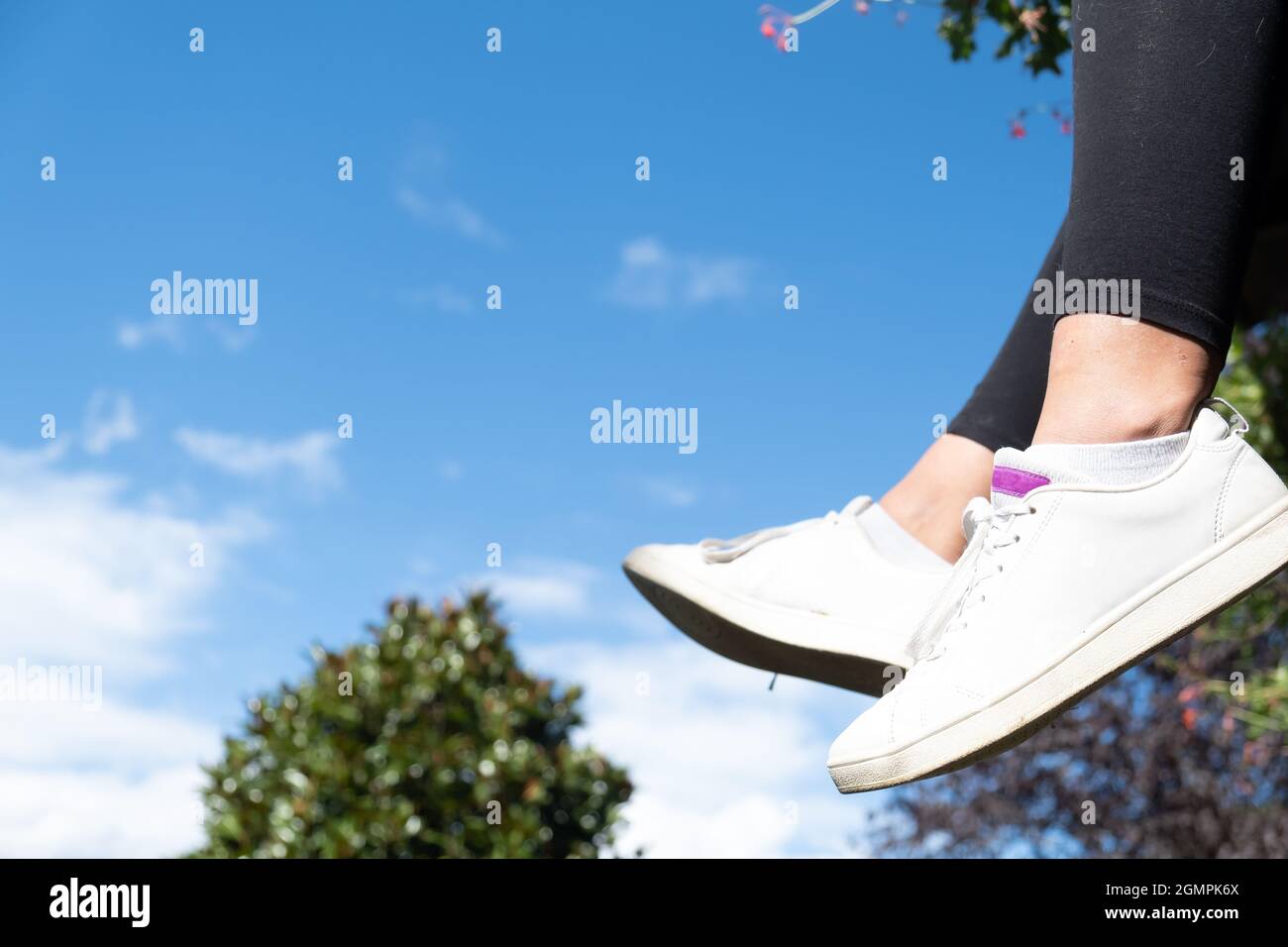 Pieds suspendus avec des sneakers pour fille, ciel en arrière-plan, beau scénario de nature avec espace de copie Banque D'Images