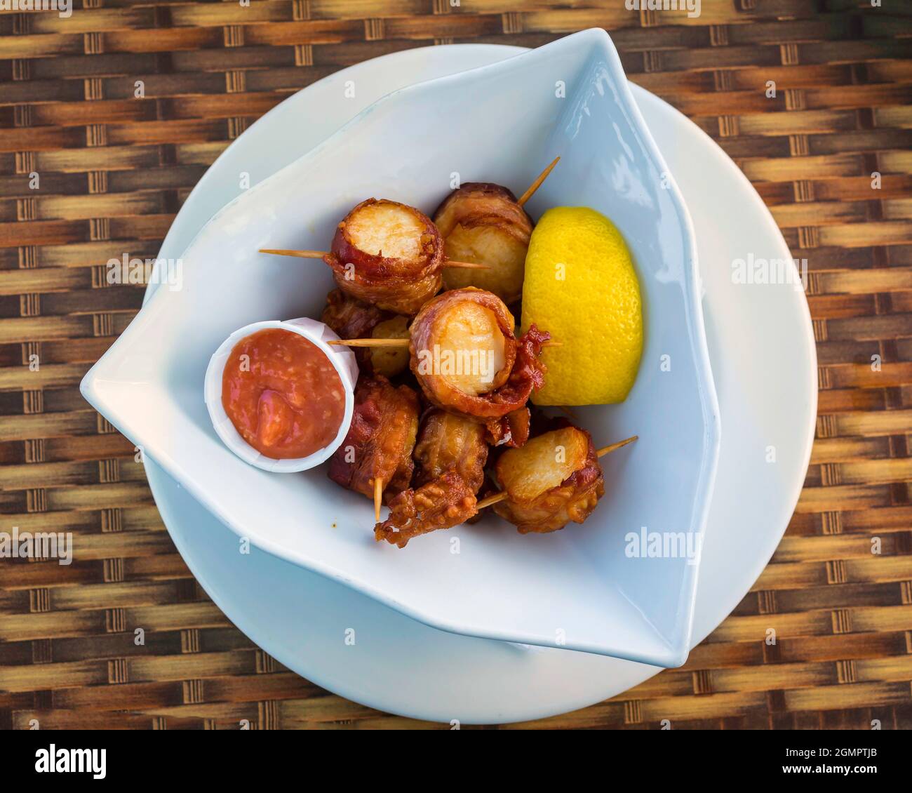 Coquilles Saint-Jacques enveloppées de bacon dans un bol avec une tranche de citron et une sauce aux fruits de mer. Banque D'Images