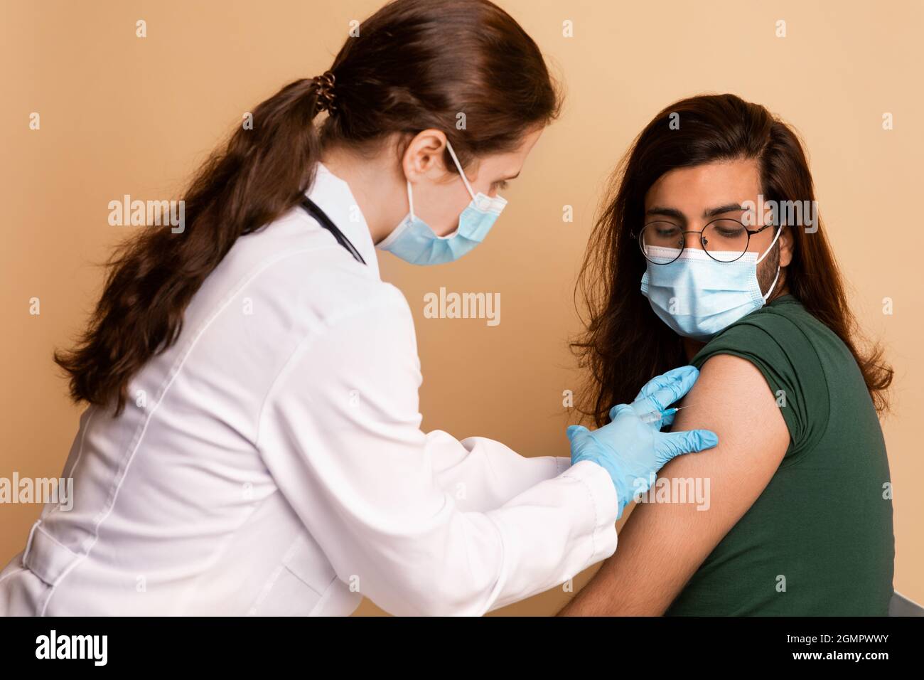 Femme médecin effectuant une injection intramusculaire pour un type arabe à la clinique Banque D'Images