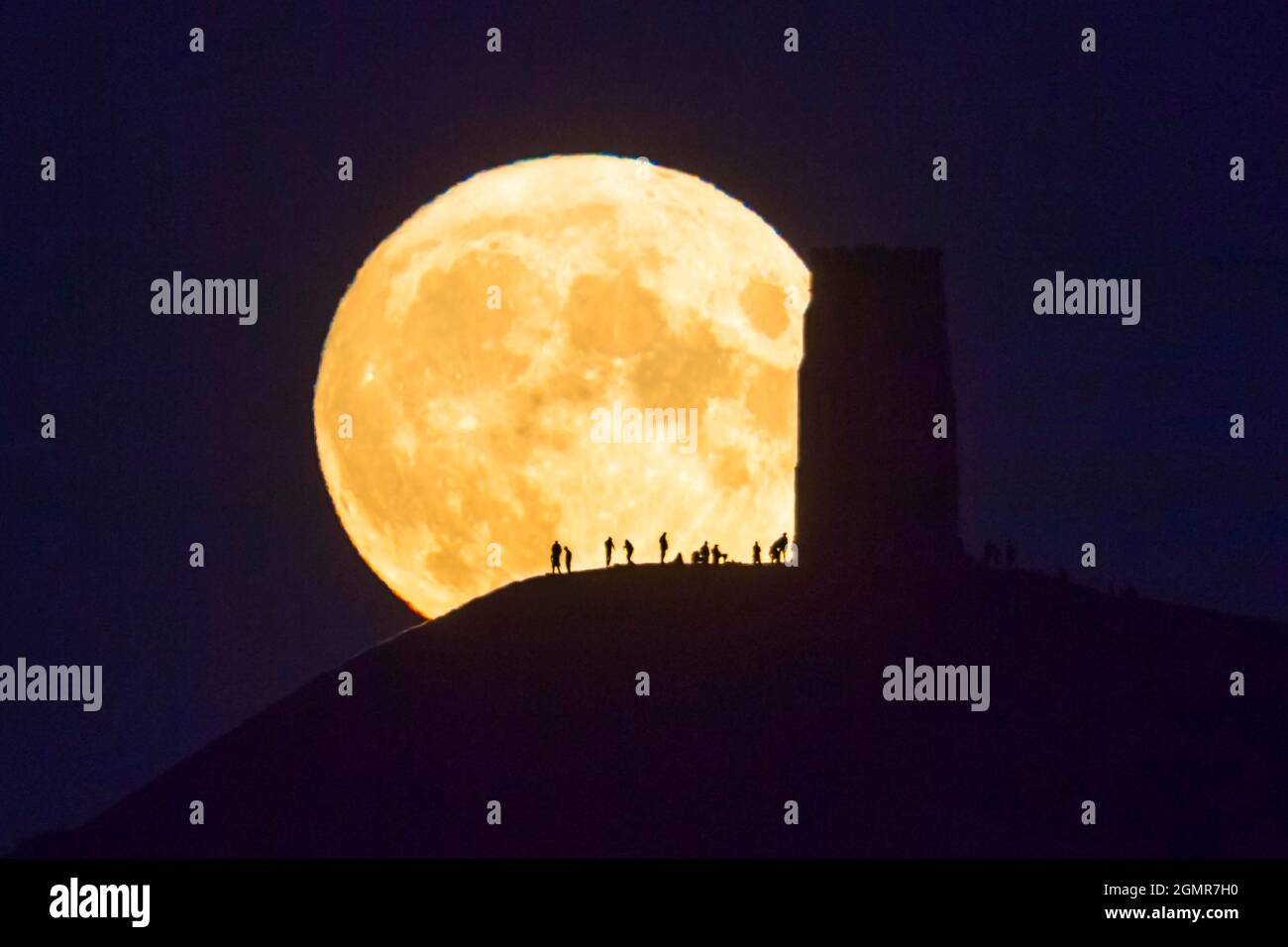 Glastonbury, Somerset, Royaume-Uni. 20 septembre 2021. Météo Royaume-Uni. La Lune de récolte complète s'élève dans le ciel clair de la nuit, derrière la Tour St Michael, sur Glastonbury Tor dans Somerset, en silhouetfiant les gens au sommet. Crédit photo : Graham Hunt/Alamy Live News Banque D'Images