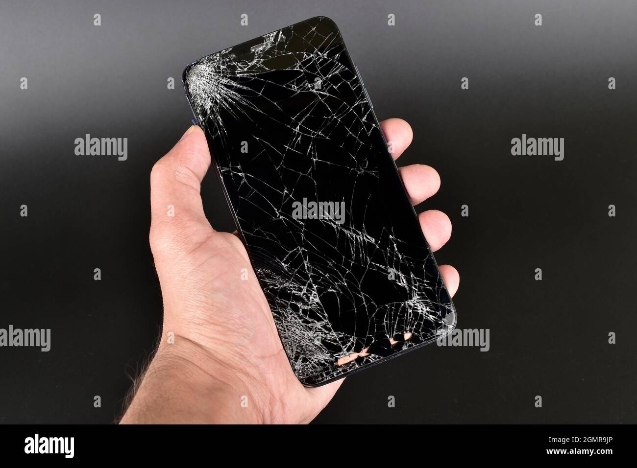 Main tenant le smartphone cassé sur un arrière-plan sombre Banque D'Images