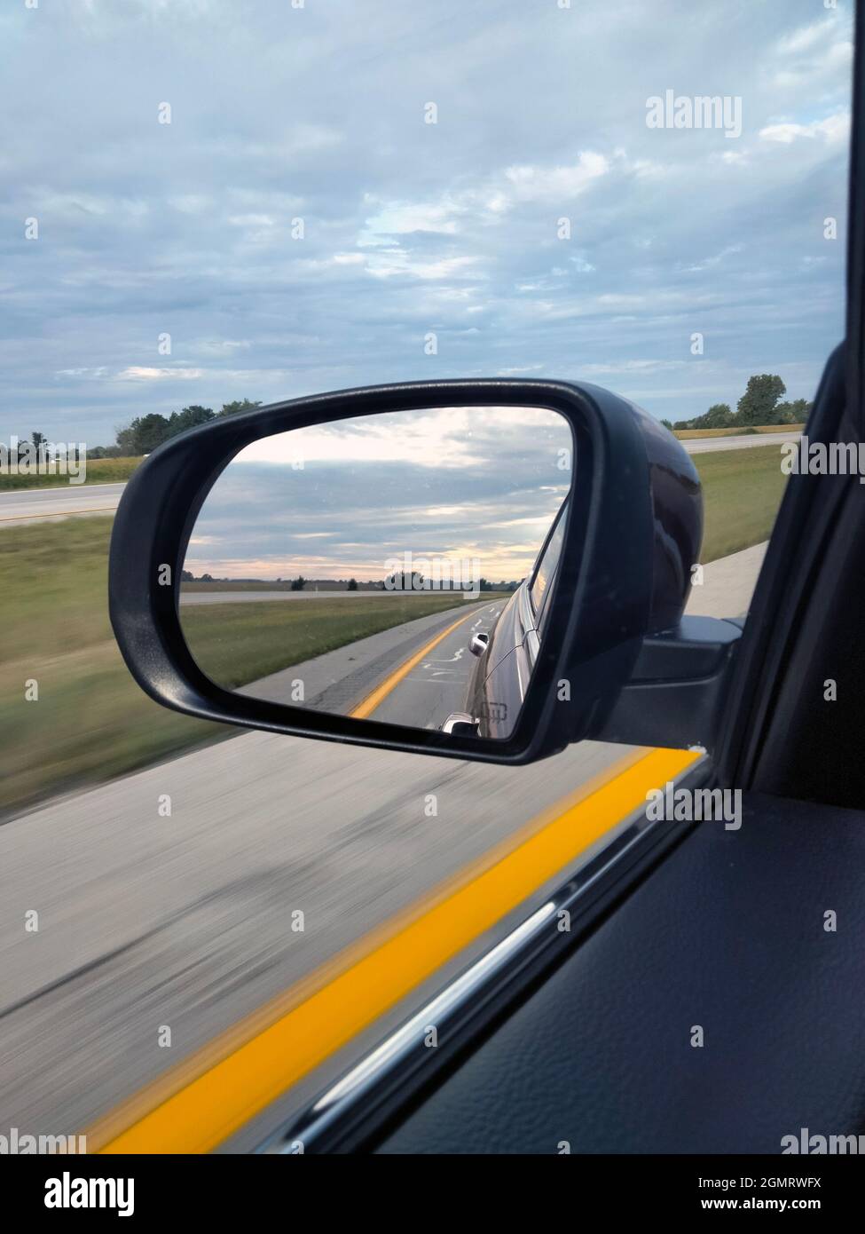 Un lever de soleil nuageux depuis le rétroviseur latéral en conduisant vers l'ouest sur une autoroute rurale dans la partie Midwestern des États-Unis Banque D'Images
