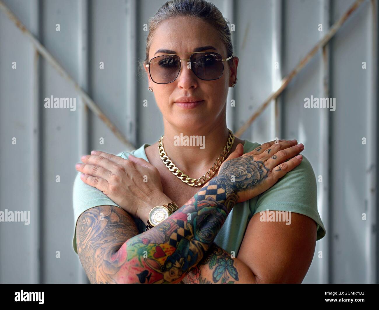 Belle confiante saine jeune femme américaine caucasienne avec des lunettes de soleil croise ses bras et affiche ses beaux tatouages artistiques colorés de bras. Banque D'Images