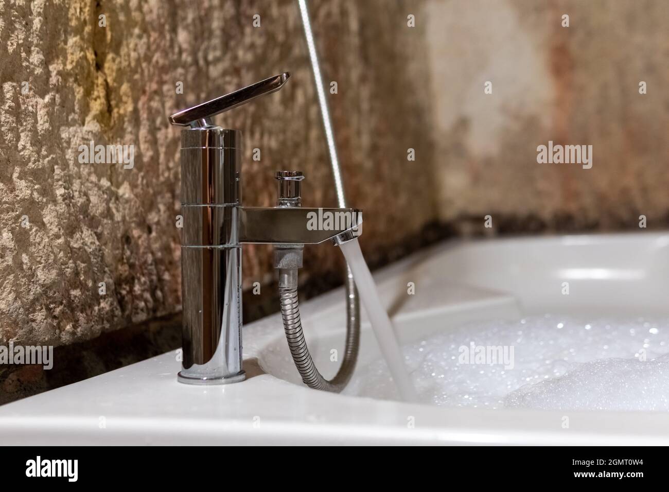 Jacuzzi, eau courante d'un robinet et un jacuzzi de remplissage, une eau mousseuse, des murs en pierre naturelle et une salle de bains d'époque Banque D'Images