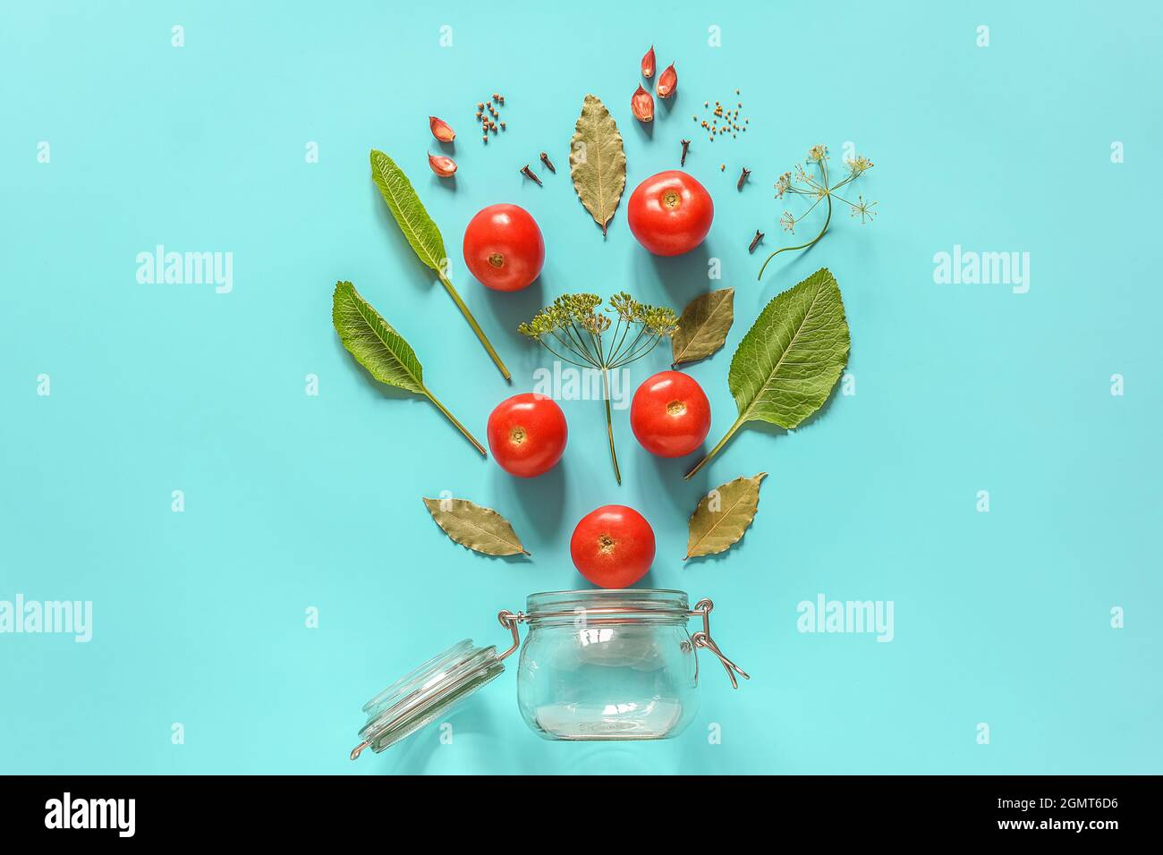 Tomates marinées. Ingrédients volants pour tomates marinées et bocal en verre sur fond bleu. Concept recette culinaire préservation des légumes en ha Banque D'Images