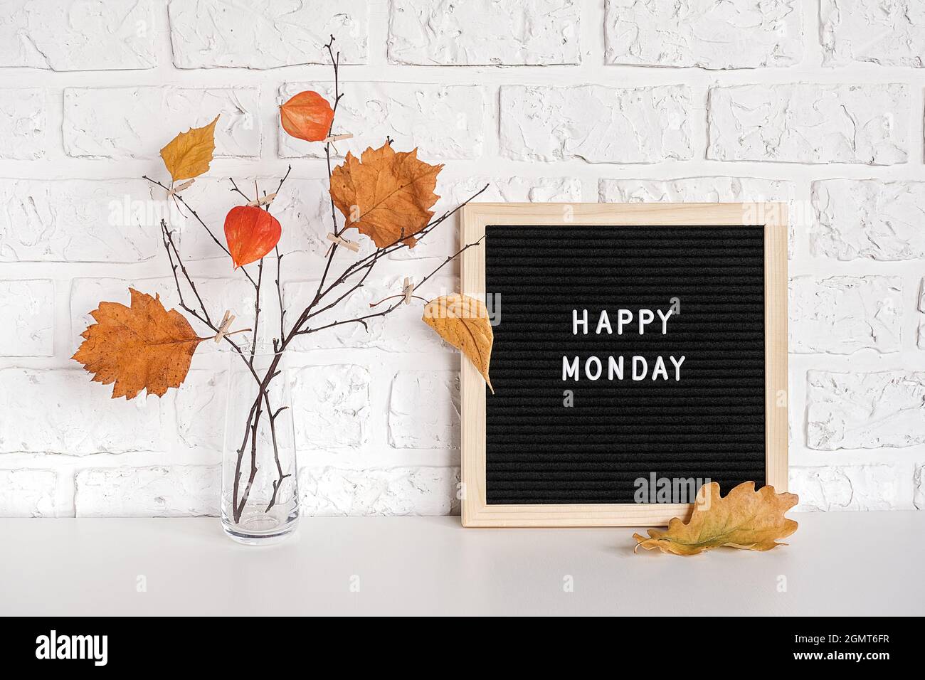Happy Monday texte sur tableau noir et bouquet de branches avec feuilles jaunes sur clotespins dans vase sur table modèle pour carte postale, voiture de voeux Banque D'Images