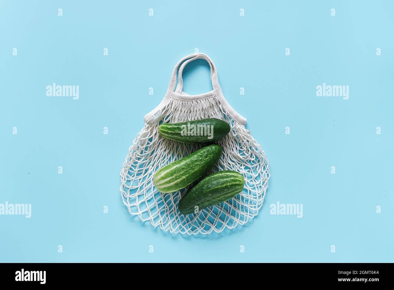 Concombres verts frais légumes sur un sac en maille écologique réutilisable sur fond bleu. Concept sans plastique et sans gaspillage. Copier l'espace vue de dessus Banque D'Images