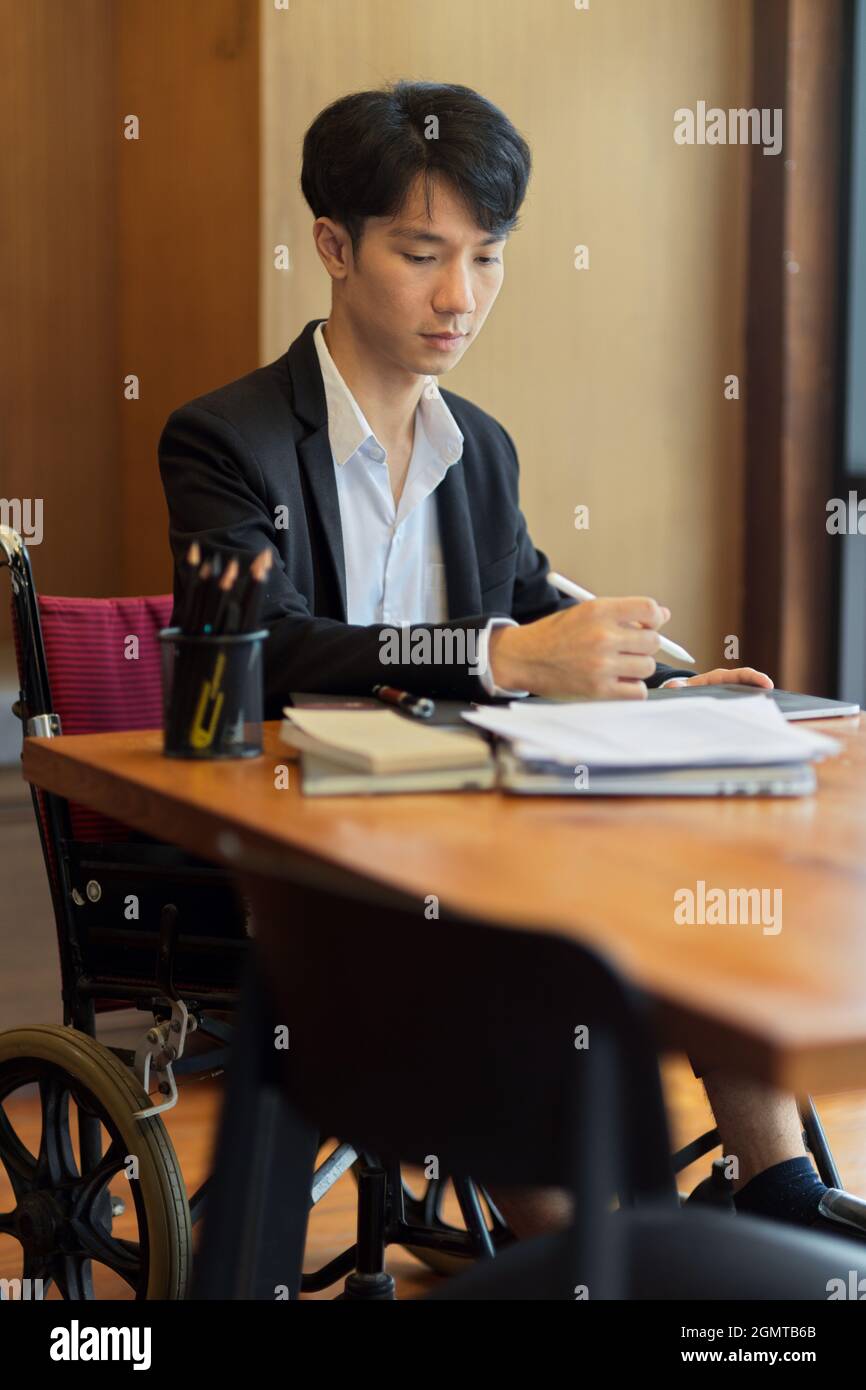 Portrait d'un jeune homme d'affaires asiatique en fauteuil roulant au bureau. Employé handicapé Banque D'Images