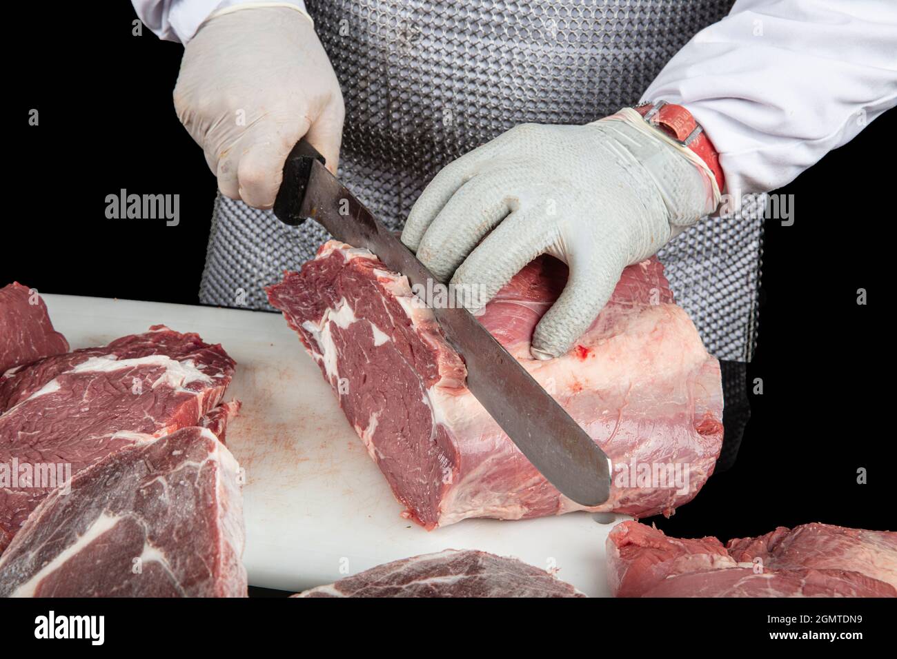 Gros plan des morceaux de viande hachés et des mains de boucher dans des gants spéciaux coupant avec un couteau. Viande de porc ou de bœuf sur la table du boucher. Le travailleur en tout Banque D'Images