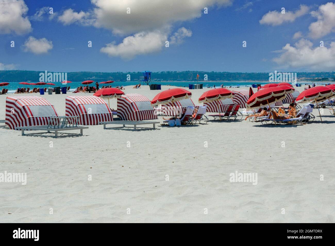 Plage de sable blanc avec parasols de plage fauteuils inclinables, personnes, bikinis, eau bleue, rayures rouges et parasols à franges victoriens, Coronado Island, CA Banque D'Images