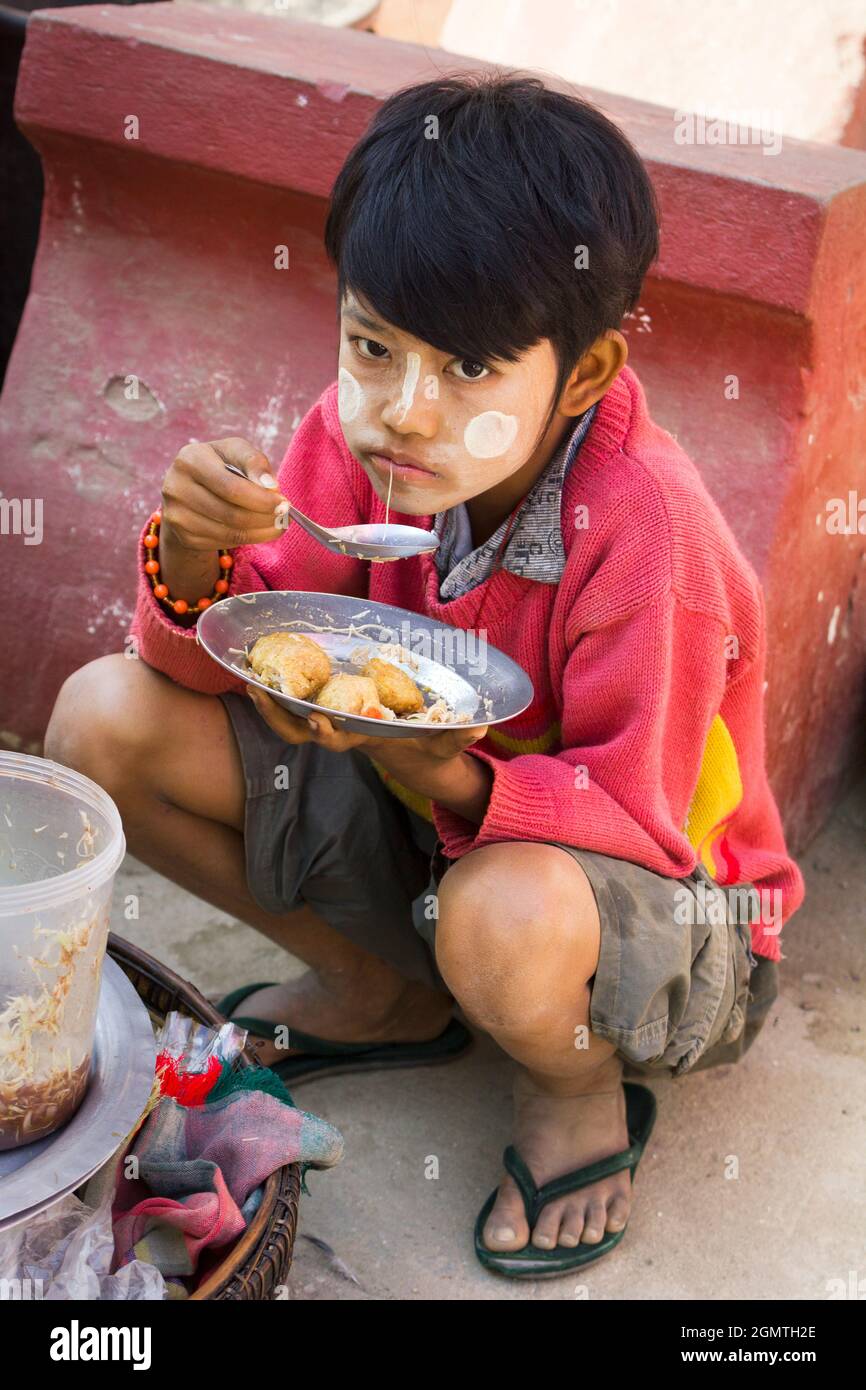 Mingun, Myanmar - 26 janvier 2013; un garçon en train de manger. Gee, ça a l'air délicieux... Le garçon porte, bien sûr, le maquillage de Thanaka pour se protéger contre Banque D'Images