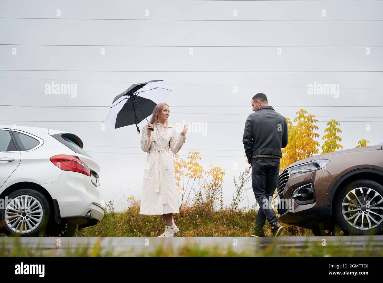 Un jeune couple sur la route à proximité de voitures dans un ciel nuageux avec pluie, se disant Au revoir l'un à l'autre. Banque D'Images