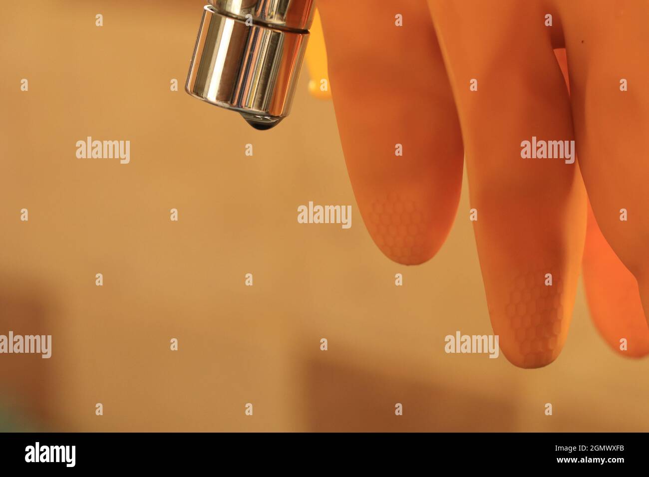 gant de lavage jaune suspendu au-dessus d'un robinet avec un goutte d'eau qui s'écoule Banque D'Images