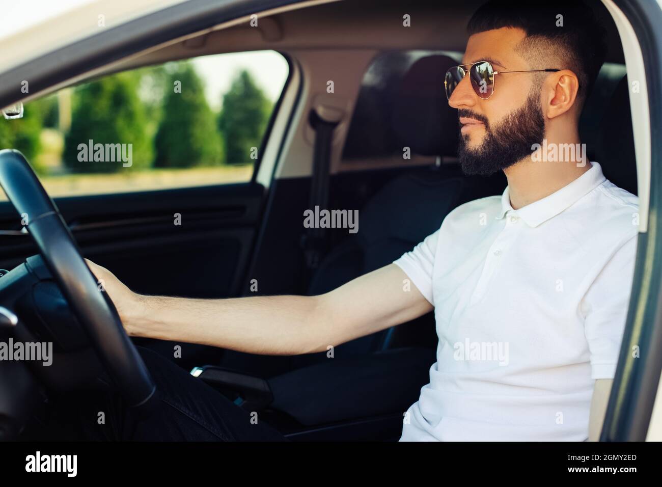 Un jeune homme heureux, portant des lunettes de soleil, assis sur le siège  du conducteur et souriant, le chauffeur de taxi écoute la musique dans la  voiture et conduit Photo Stock -
