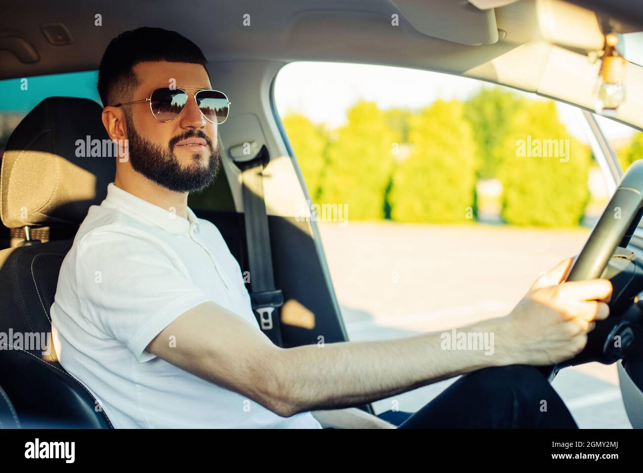 Un jeune homme heureux, portant des lunettes de soleil, assis sur le siège  du conducteur et souriant, le chauffeur de taxi écoute la musique dans la  voiture et conduit Photo Stock -