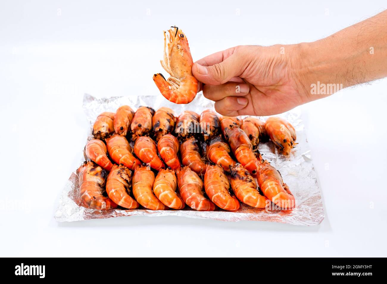 Gros plan une main humaine ramasse les crevettes de rivière grillées d'une pile sur du papier aluminium sur fond blanc. Banque D'Images Gros plan une main humaine ramasse les crevettes de rivière grillées d'une pile sur du papier aluminium sur fond blanc. Banque D'Images