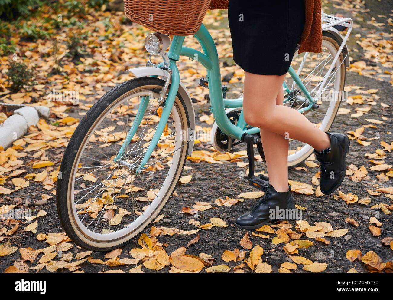 Gros plan sur les jambes des femmes dans des chaussures élégantes et un vélo  bleu sur la rue d'automne. Jeune femme debout à vélo sur l'asphalte avec  des feuilles jaunes tout en
