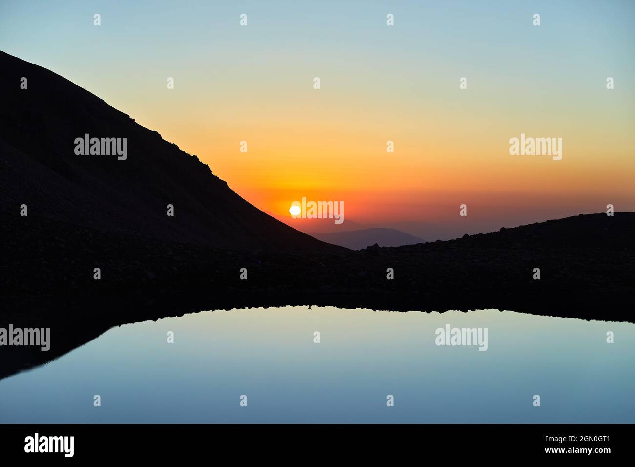Magnifique paysage de grand lac et silhouette de montagnes à la lumière du coucher du soleil brillent dans les montagnes Tien Shan, Kazakhstan. Banque D'Images