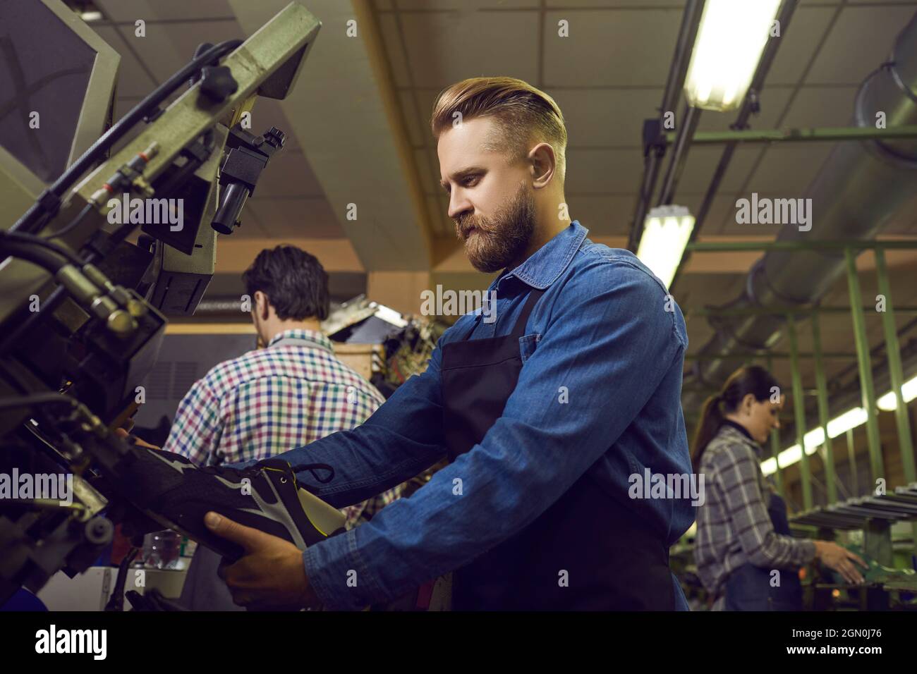 Flux de travail. Travailleur de l'usine de chaussures masculin concentré qui fabrique des chaussures de sport sur son lieu de travail. Banque D'Images