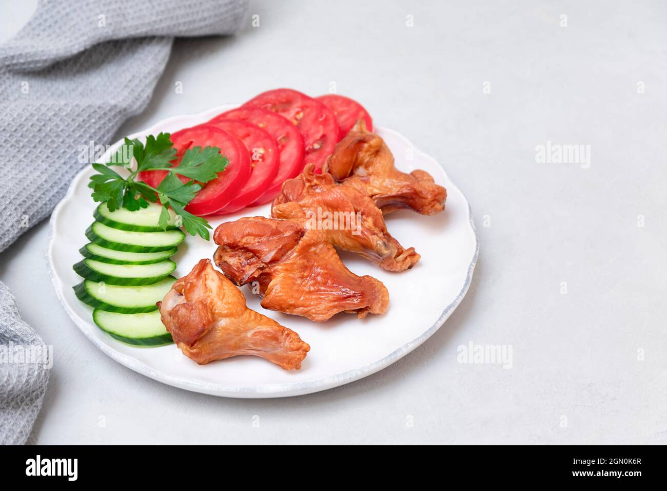 Ailes de poulet fumé sur une assiette blanche avec salade latérale sur fond gris neutre, espace de copie Banque D'Images